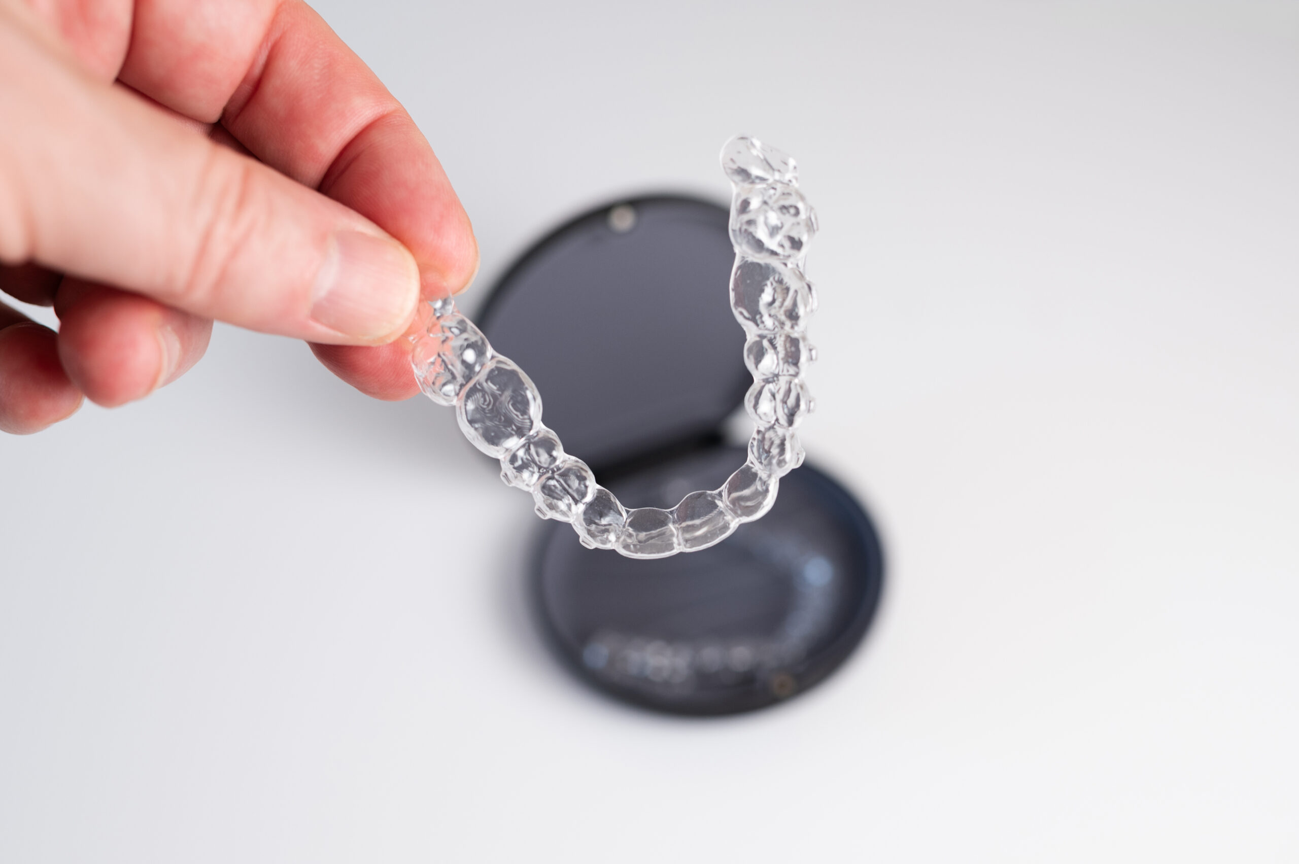 A clear ELVYTA aligner held over its storage case